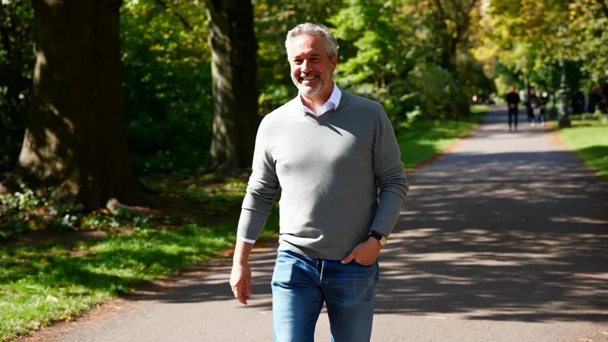 A man walking through a sunlit park, relaxed and rested
